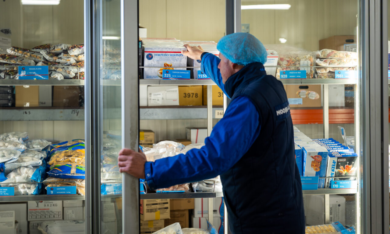 medewerker van mooijer die struint in het assortiment en torpedo garnalen vasthoudt en bekijkt.
